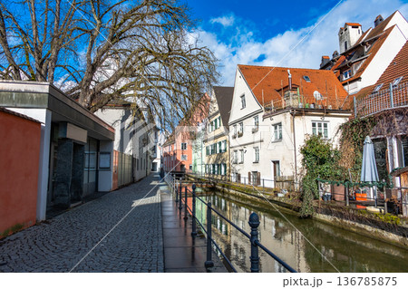 Colourful houses line the streets of Memmingen, Germany, alongside tranquil water canals. A clear blue sky enhances the picturesque scene. Colourful houses line the streets of Memmingen, Germany, alongside tranquil water canals. A clear blue sky enhances the picturesque scene. 136785875