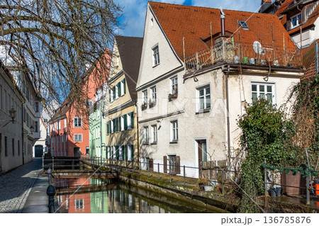 Colourful houses line the streets of Memmingen, Germany, alongside tranquil water canals. A clear blue sky enhances the picturesque scene. Colourful houses line the streets of Memmingen, Germany, alongside tranquil water canals. A clear blue sky enhances the picturesque scene. 136785876