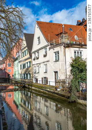 Colourful houses line the streets of Memmingen, Germany, alongside tranquil water canals. A clear blue sky enhances the picturesque scene. Colourful houses line the streets of Memmingen, Germany, alongside tranquil water canals. A clear blue sky enhances the picturesque scene. 136785877