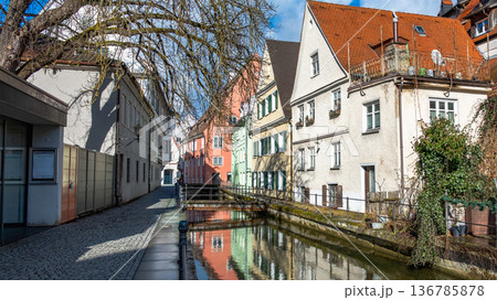 Colourful houses line the streets of Memmingen, Germany, alongside tranquil water canals. A clear blue sky enhances the picturesque scene. 136785878