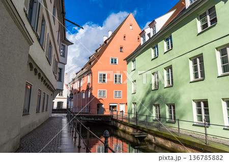 Colourful houses line the streets of Memmingen, Germany, alongside tranquil water canals. A clear blue sky enhances the picturesque scene. 136785882