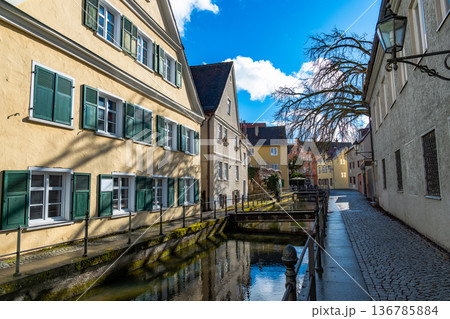 Colourful houses line the streets of Memmingen, Germany, alongside tranquil water canals. A clear blue sky enhances the picturesque scene. Colourful houses line the streets of Memmingen, Germany, alongside tranquil water canals. A clear blue sky enhances the picturesque scene. 136785884
