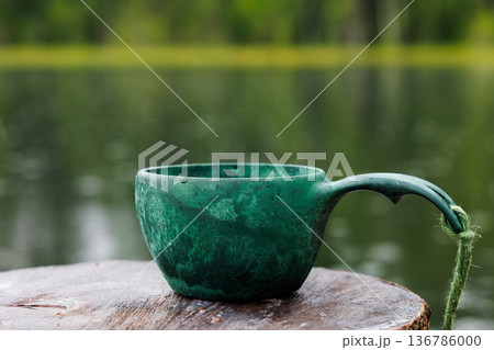 Serene green cup rests on wooden stump by tranquil lake surrounded by lush greenery Serene green cup rests on wooden stump by tranquil lake surrounded by lush greenery 136786000