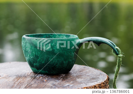 Crafted from nature, a rustic green cup rests peacefully on a wooden stump by a serene lake 136786001