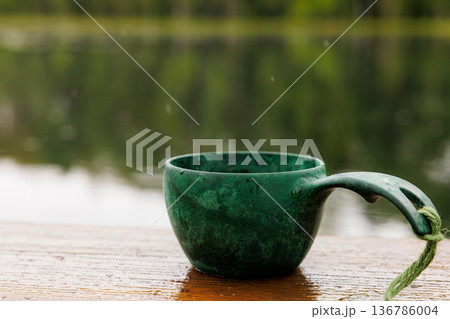 Relaxing by the serene lake with a warm cup of tea as raindrops dance on the surface Relaxing by the serene lake with a warm cup of tea as raindrops dance on the surface 136786004