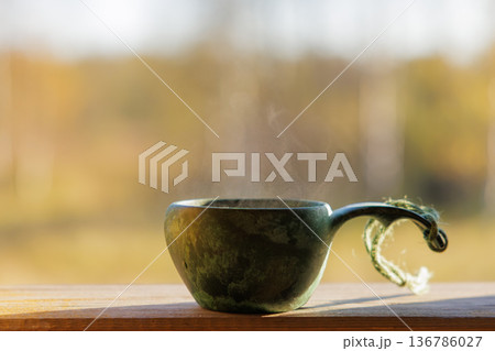 Warm cup of herbal tea resting on a wooden table, inviting tranquility in a serene outdoor setting Warm cup of herbal tea resting on a wooden table, inviting tranquility in a serene outdoor setting 136786027