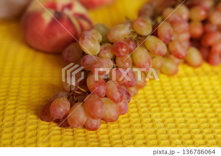 Fresh grapes glistening in natural light beside vibrant peaches on a sunny yellow background 136786064