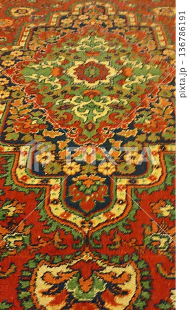 Close-up of an oriental rug featuring a vibrant pattern with red, green, and blue hues. The intricate floral and geometric motifs create a rich tapestry ideal for design inspiration. Close-up of an oriental rug featuring a vibrant pattern with red, green, and blue hues. The intricate floral and geometric motifs create a rich tapestry ideal for design inspiration. 136786191