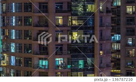 Windows of the multi-storey building of glass and steel lighting inside and moving people within timelapse 136787210