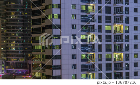 Windows of the multi-storey building of glass and steel lighting inside and moving people within timelapse 136787216