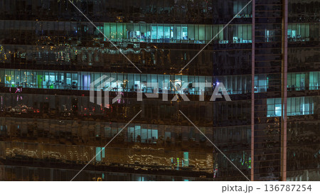Windows of the multi-storey building of glass and steel lighting inside and moving people within timelapse 136787254