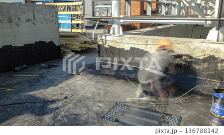 Roofer installing roofing felt with heating and melting of bitumen roll by torch on flame during roof repair timelapse 136788142