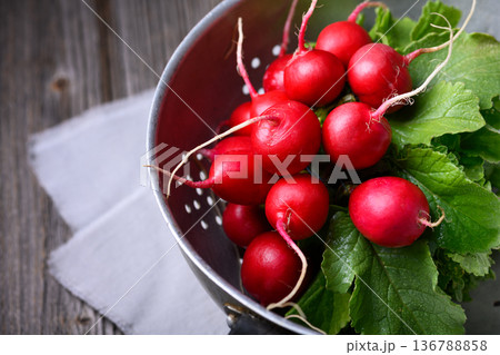 Radishes with foliage in metal bowl on linen cloth 136788858