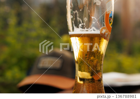 Golden beer glass shining in the sunlight with a casual hat nearby on a warm day outdoors 136788981