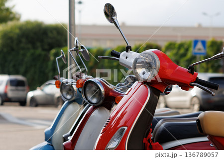 Vintage scooters parked in a sunny urban area next to lush greenery on a pleasant afternoon Vintage scooters parked in a sunny urban area next to lush greenery on a pleasant afternoon 136789057