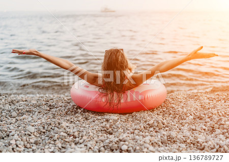 Woman beach summer young woman relaxing on inflatable ring at pebble shore during sunset 136789727