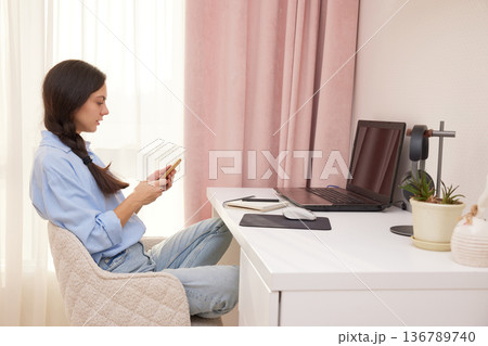 Woman playing with smartphone at desk, avoiding work on laptop in home office 136789740