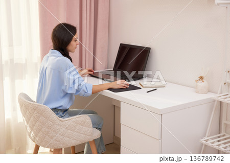 Young woman confidently working on a laptop computer in her modern home office 136789742