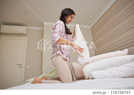 Young woman making bed, changing pillow cover during morning routine Young woman making bed, changing pillow cover during morning routine 136789745
