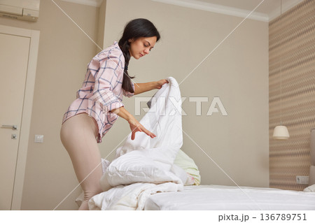 Woman making her bed, tidying up bedroom for a fresh start to the day Woman making her bed, tidying up bedroom for a fresh start to the day 136789751