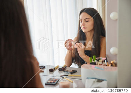 Woman applying cosmetic lip liner, looking in a mirror at her reflection 136789770