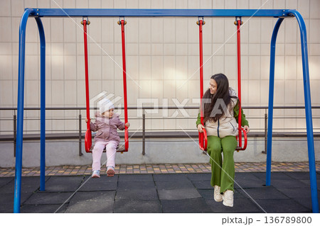 Mother and daughter swinging, having fun and bonding at the playground Mother and daughter swinging, having fun and bonding at the playground 136789800
