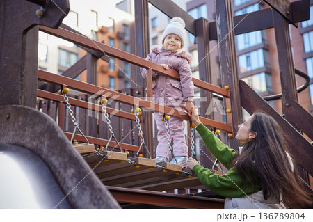 Mother and child playing on a playground bridge, holding hands and smiling Mother and child playing on a playground bridge, holding hands and smiling 136789804