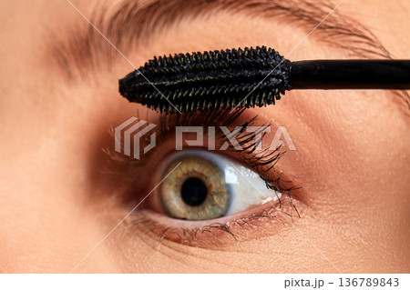 Woman applying black mascara from applicator brush to an eyelid and long eyelashes Woman applying black mascara from applicator brush to an eyelid and long eyelashes 136789843
