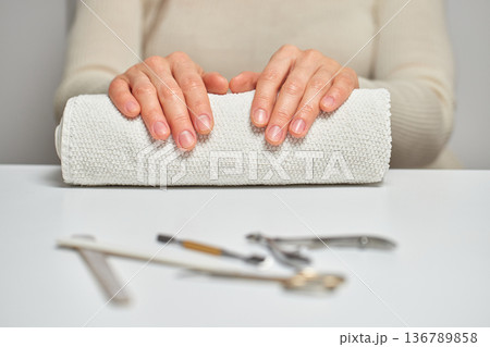 Woman's hands resting on a rolled towel, with manicure tools ready on a white table 136789858