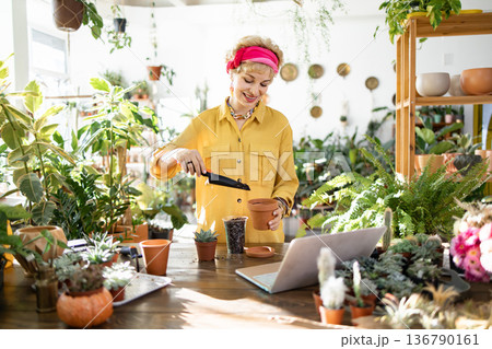 A woman in a yellow shirt is planting a succulent in a terracotta pot, enjoying the process A woman in a yellow shirt is planting a succulent in a terracotta pot, enjoying the process 136790161