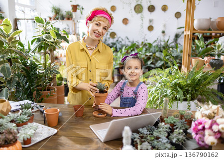 A woman and a young girl smile while working with plants, creating a heartwarming scene of family and nature A woman and a young girl smile while working with plants, creating a heartwarming scene of family and nature 136790162