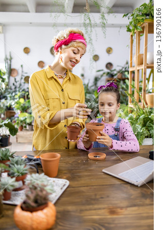 A mother and daughter enjoy a gardening activity, potting a succulent plant together at a wooden table A mother and daughter enjoy a gardening activity, potting a succulent plant together at a wooden table 136790166