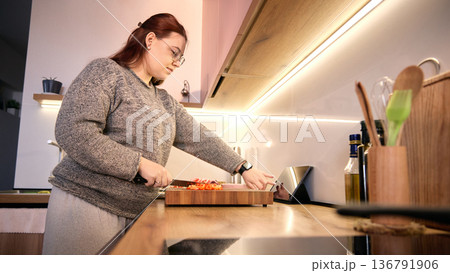 Wide angle view of woman using tablet while preparing chopped vegetables in modern kitchen. Wide angle view of woman using tablet while preparing chopped vegetables in modern kitchen. 136791906