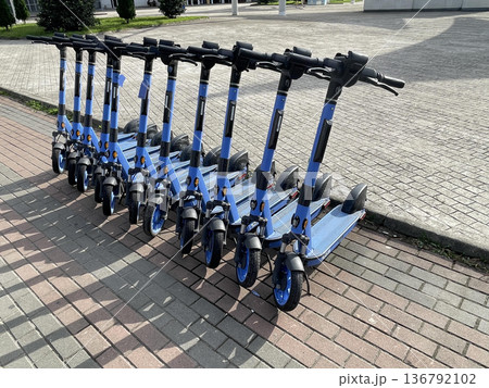 A row of scooters sits on the sidewalk for rent on a sunny day 136792102