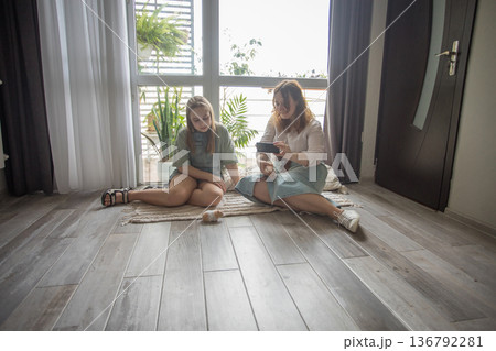 A mother and her daughter sit on a rug with hamster in a well-lit room. They are focused A mother and her daughter sit on a rug with hamster in a well-lit room. They are focused 136792281