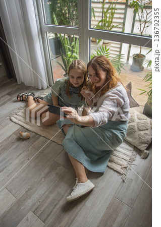 A mother and her daughter sit on a rug with hamster in a well-lit room. They are focused 136792355