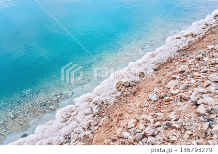 Sand covered with crystalline salt on shore of Dead Sea, turquoise blue water near - typical scenery at Ein Bokek beach, Israel 136793279