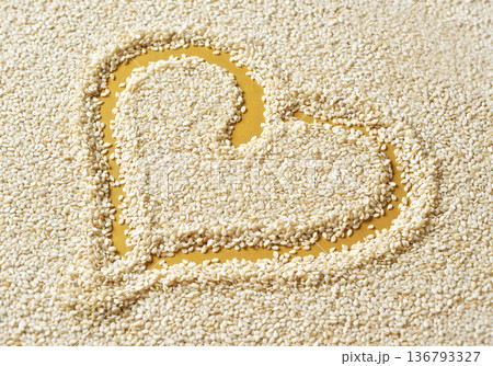 White sesame seeds on yellow desk, heart shape drawn with finger inside 136793327