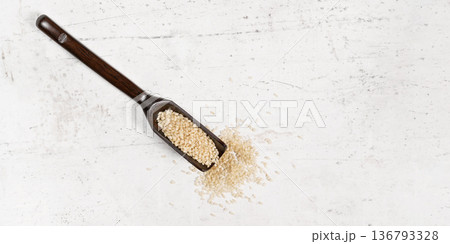 White sesame - Sesamum indicum - seeds in small wooden spoon on white stone like board, view from above, space for text right side White sesame - Sesamum indicum - seeds in small wooden spoon on white stone like board, view from above, space for text right side 136793328