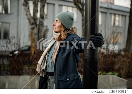 Woman enjoys cool weather while standing near a lamppost in an urban setting during autumn Woman enjoys cool weather while standing near a lamppost in an urban setting during autumn 136793914