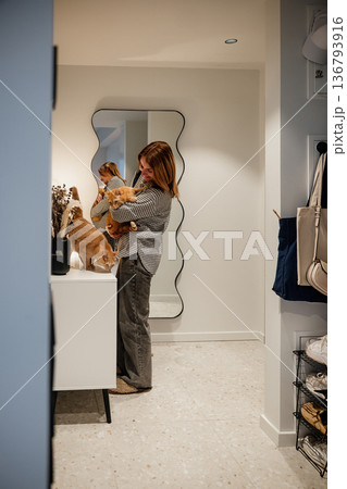 Woman holding dog in a hall with a mirror and a table during evening time at home 136793916