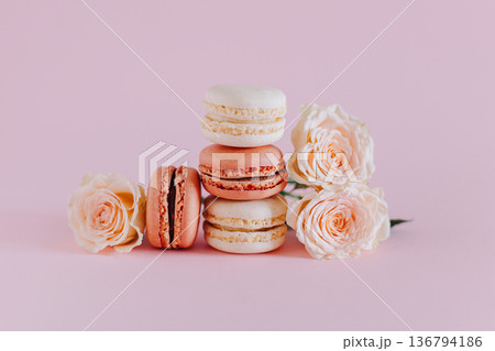 Tasty french macarons with tender rose flowers on a pink pastel background. Tasty french macarons with tender rose flowers on a pink pastel background. 136794186