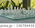 Glass chess pieces on a glass board in a room against the window with green plants and summer view. Close up. Copy space at the bottom. The concept of hobby and leisure. Real photo shot at eye level. 136794438