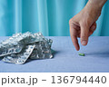 The fair-skinned woman's hand takes the last pill from the table. A pile of empty blister packs sits against a plain background. The overuse of medications, living on medication, drug shortages. 136794440