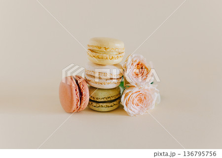 Tasty french macarons with tender rose flowers on a peach pastel background. Tasty french macarons with tender rose flowers on a peach pastel background. 136795756