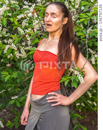 Young woman sneezes in the park against the background of a flowering tree. Allergy to pollen concept. Young woman sneezes in the park against the background of a flowering tree. Allergy to pollen concept. 136797126