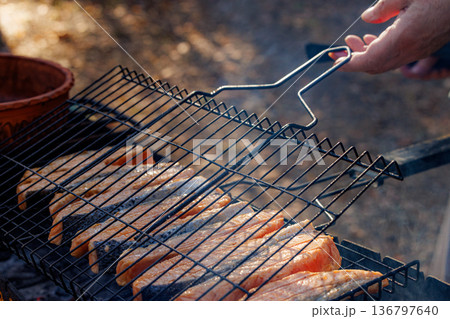 Enjoying a sunny afternoon grilling fresh salmon over an outdoor fire with friends in a beautiful setting Enjoying a sunny afternoon grilling fresh salmon over an outdoor fire with friends in a beautiful setting 136797640