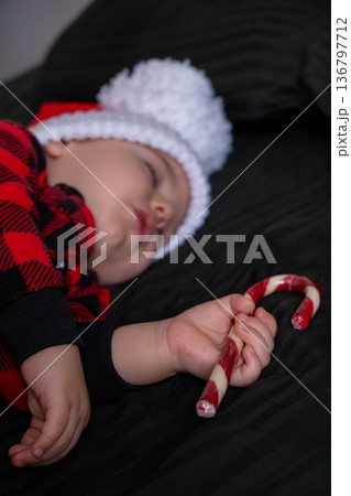 Sleeping baby in santa hat holding candy cane Sleeping baby in santa hat holding candy cane 136797712