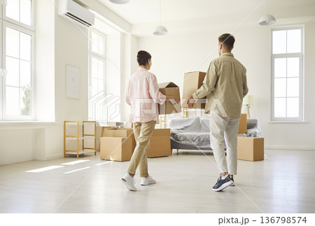 Couple carrying boxes while moving into bright new apartment with minimal decor Couple carrying boxes while moving into bright new apartment with minimal decor 136798574
