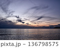 Seascape at dusk with wispy clouds, orange sunset glow and dark coastline, calm ocean and evening sky 136798575